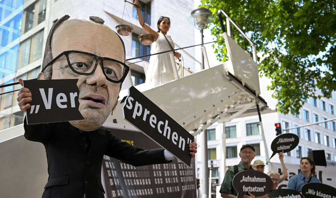 An activist depicting Chancellor Friedrich Merz shows a broken "promise" lettering in a symbolic protest action for the continuation of visa issuance under the admission programs for vulnerable Afghans, in connection with the first wave of lawsuits against the Federal Foreign Office and the suspending and reassess all refugee programs of the German government, in Berlin, Germany on June 20, 2025. (REUTERS/File)