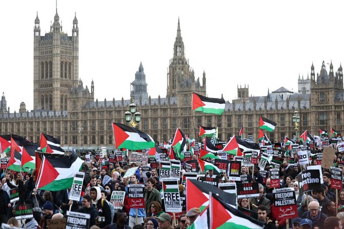 Protesters hold placards and wave Palestinian flags as they walk over Westminster Bridge with the Palace of Westminster, home of the Houses of Parliament behind during a 'March For Palestine' in London on October 28, 2023. (AFP)