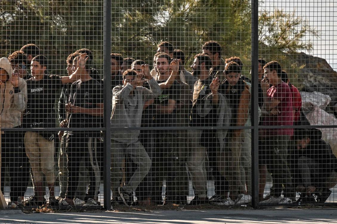Migrants stand behind a fence as they are gathered by Greek coast guard officers after disembarking from a cargo ship, in the port of Lavrio, south of Athens, July 10, 2025. (AFP)