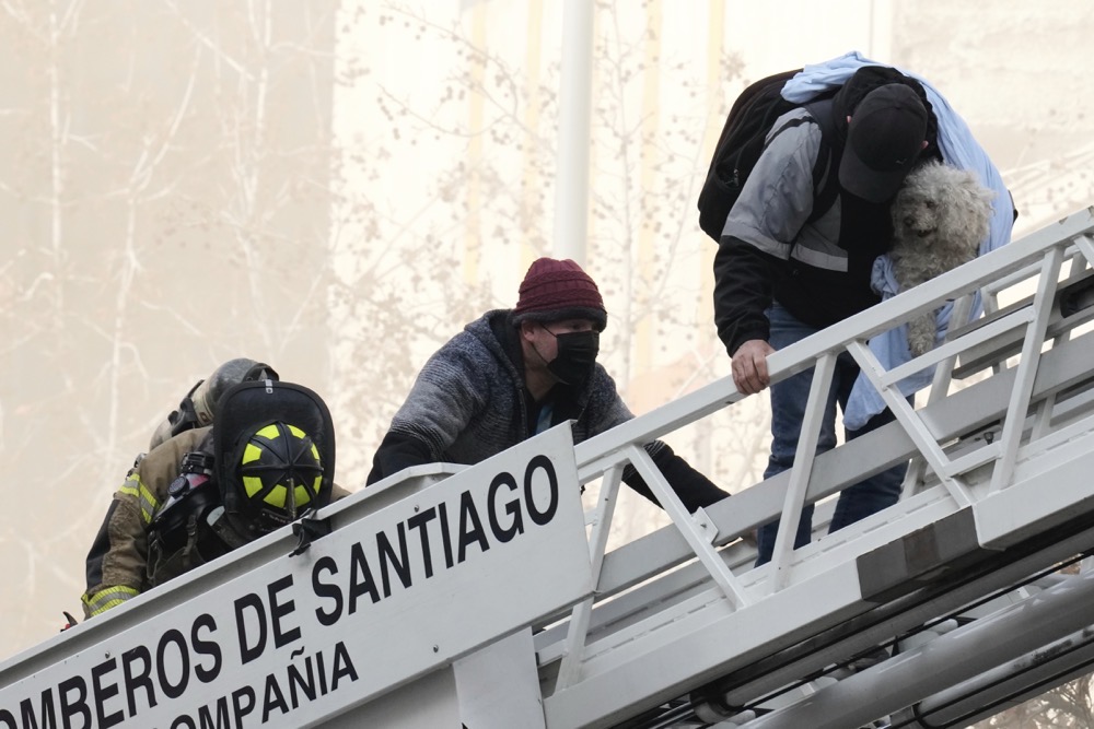 Firefighters rescue people and a dog that were trapped inside a burning building in Santiago. (AP)
