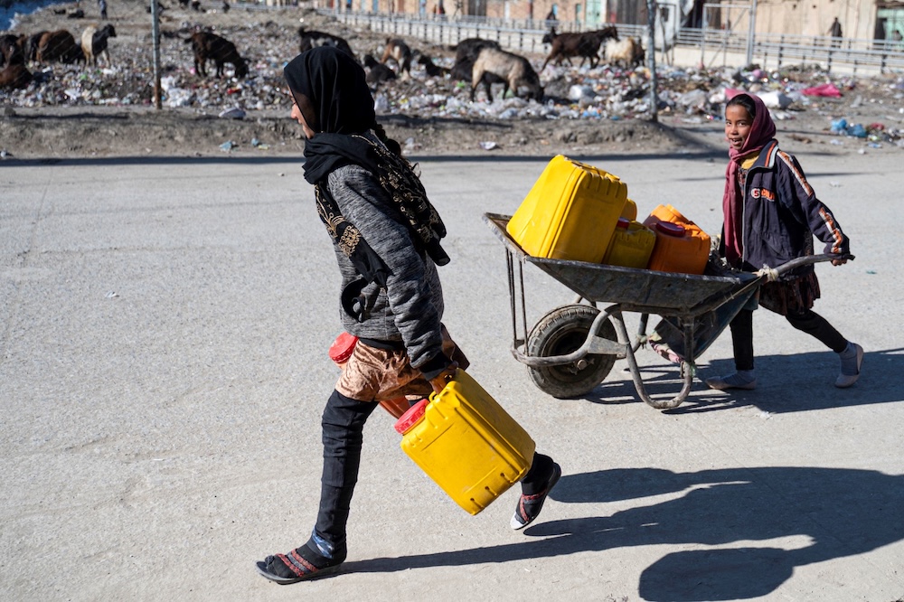 Afghan girls carry water cans on a wheelbarrow along a street in Kabul on Jan. 3, 2023. (AFP)