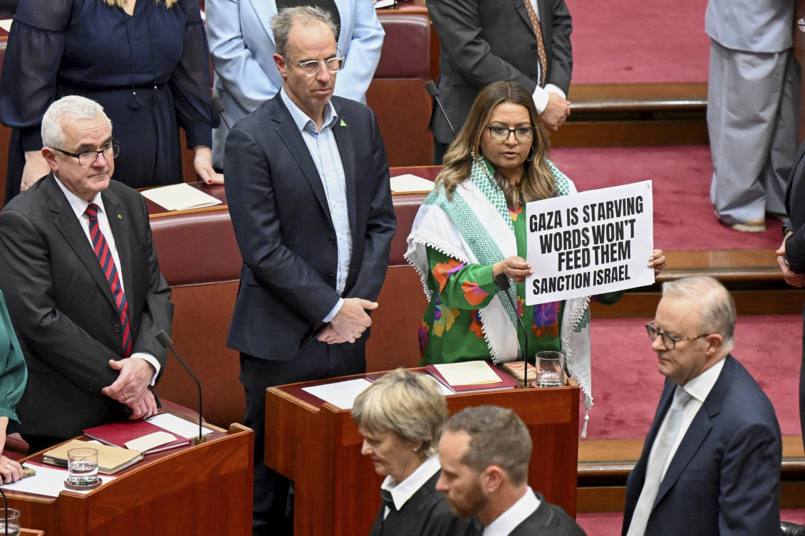Greens Senator Mehreen Faruqi holds a placard as Australian Prime Minister Anthony Albanese walks in the Senate chamber for the opening of the 48th Federal Parliament at Parliament House in Canberra on July 22, 2025. (AAP Image via AP)