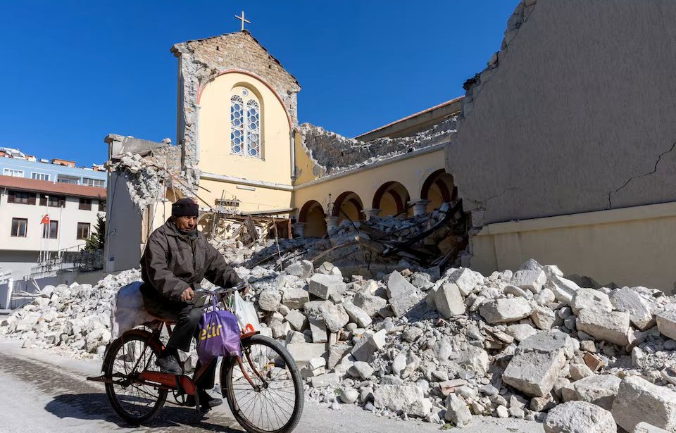 A man cycles his bike beside a collapsed Roman Catholic church in the aftermath of an earthquake in Iskenderun, a coastal town of Hatay province, Turkey, Feb. 14, 2023. (Reuters)
