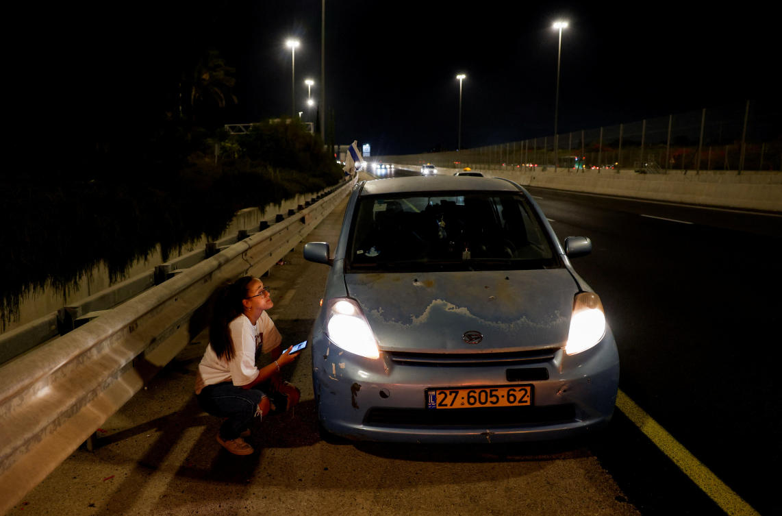A woman takes cover behind a car while sirens sound in response to a missile launched from Yemen toward Israel that was intercepted. (Reuters)