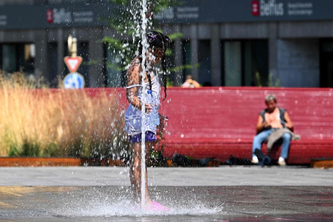A girl cools off at the water jets of a public fountain as outside temperatures reach 37 degrees celsius in Brussels on July 1, 2025. (AFP)