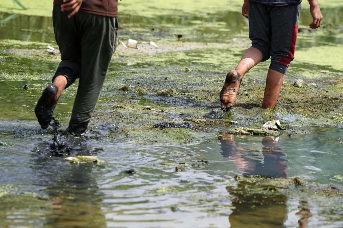Iraqi children walk in an almost dried-up stream in Mishkhab, in Iraq's Najaf province, where years of drought have negatively affected the fauna and flora of the region, May 24, 2025. (AFP)