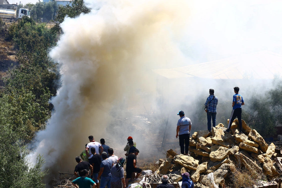 Turkiye has been hit by dozens of wildfires daily since late June. Above, people stand next to smoke rising from the wildfire in the Aksu district of Antalya in southern Turkiye on July 25, 2025. (Reuters)