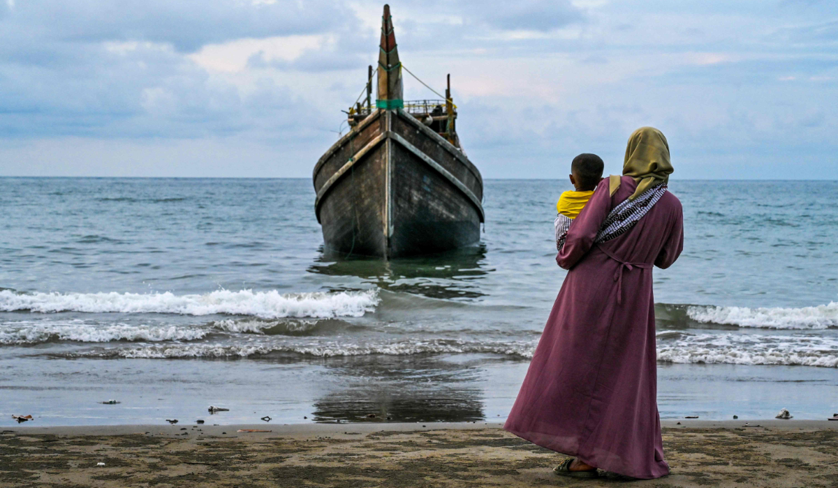 A woman with her child looks at a boat which carried Rohingya refugees to the Laweueng beach in Pidie. (AFP)