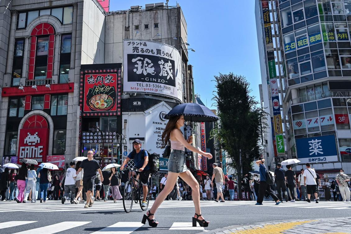 A woman carries an umbrella to shelter from the sun as pedestrians cross a street in the Kabukicho entertainment area of Shinjuku in central Tokyo on July 29, 2025. (AFP)