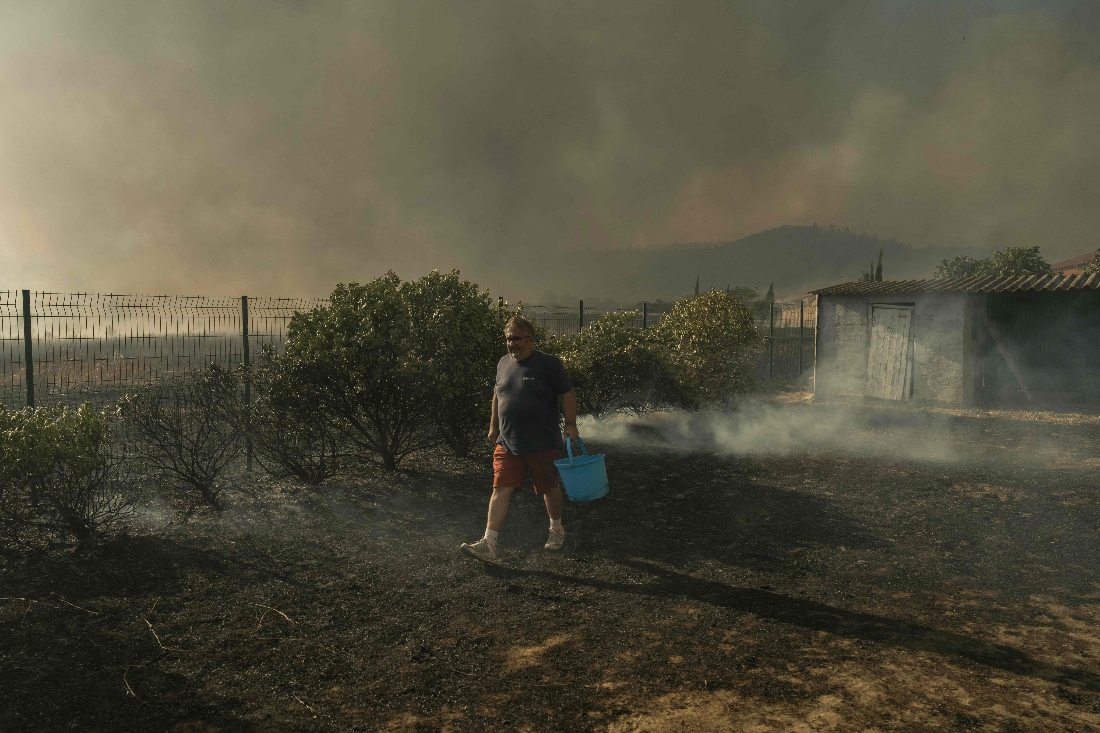 A resident carries a water bucket to extinguish a wildfire in Tournissan, southwestern France. (AFP)