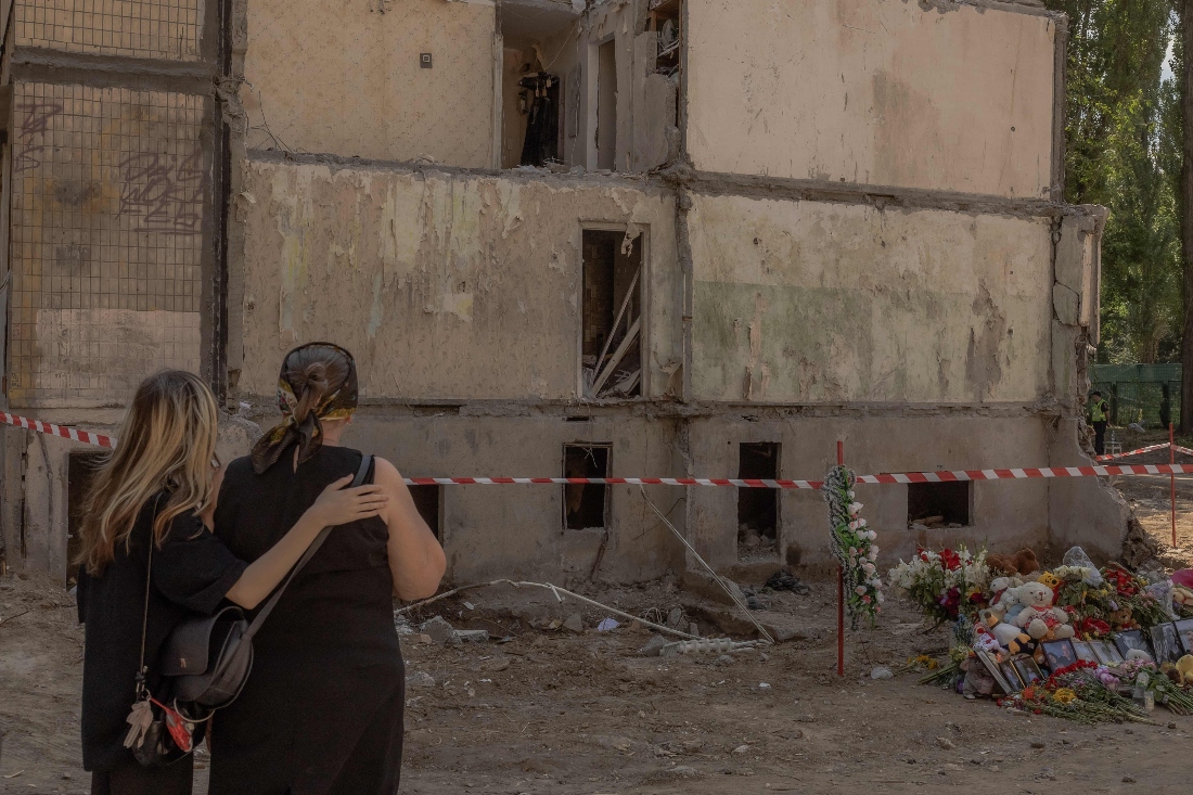 Women stand next to flowers, children's toys, and portraits placed in memory of victims at the site of a nine-storey residential building destroyed following a recent Russian missile strike in Kyiv, Ukraine. (AFP)