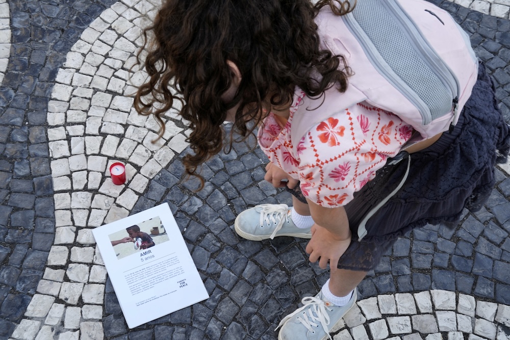 A child looks at a photograph of Amir, a five-year-old Palestinian boy who was killed while collecting food aid in Gaza, during a protest in downtown Lisbon on Aug. 7, 2025. (AP)