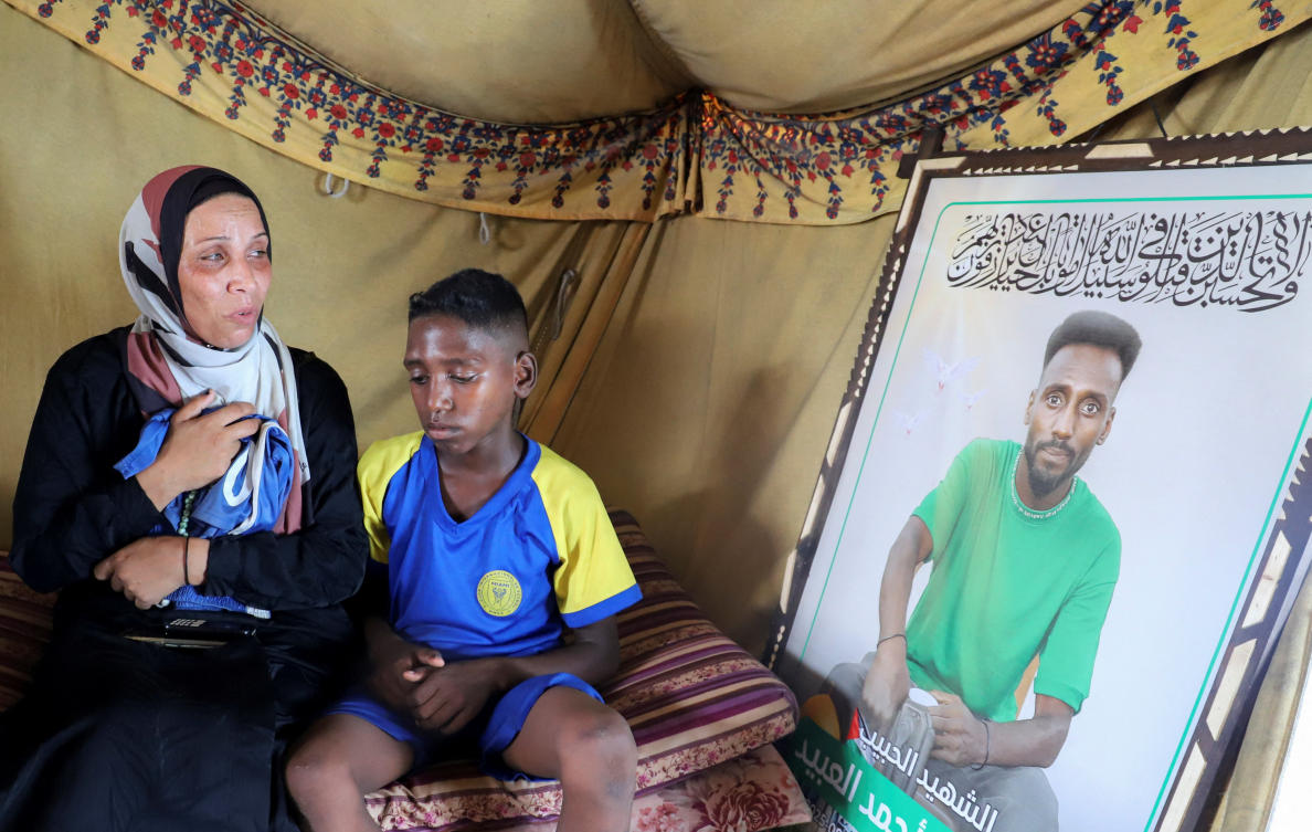 Doaa, the widow of late soccer player Suleiman Al-Obeid, known as the “Palestinian Pele,” who was killed by an Israeli strike targeting people waiting for humanitarian aid, according to the Palestine Football Association, looks at his picture while holding his shorts, as her son sits beside her inside their tent in Gaza City August 9, 2025. (Reuters)