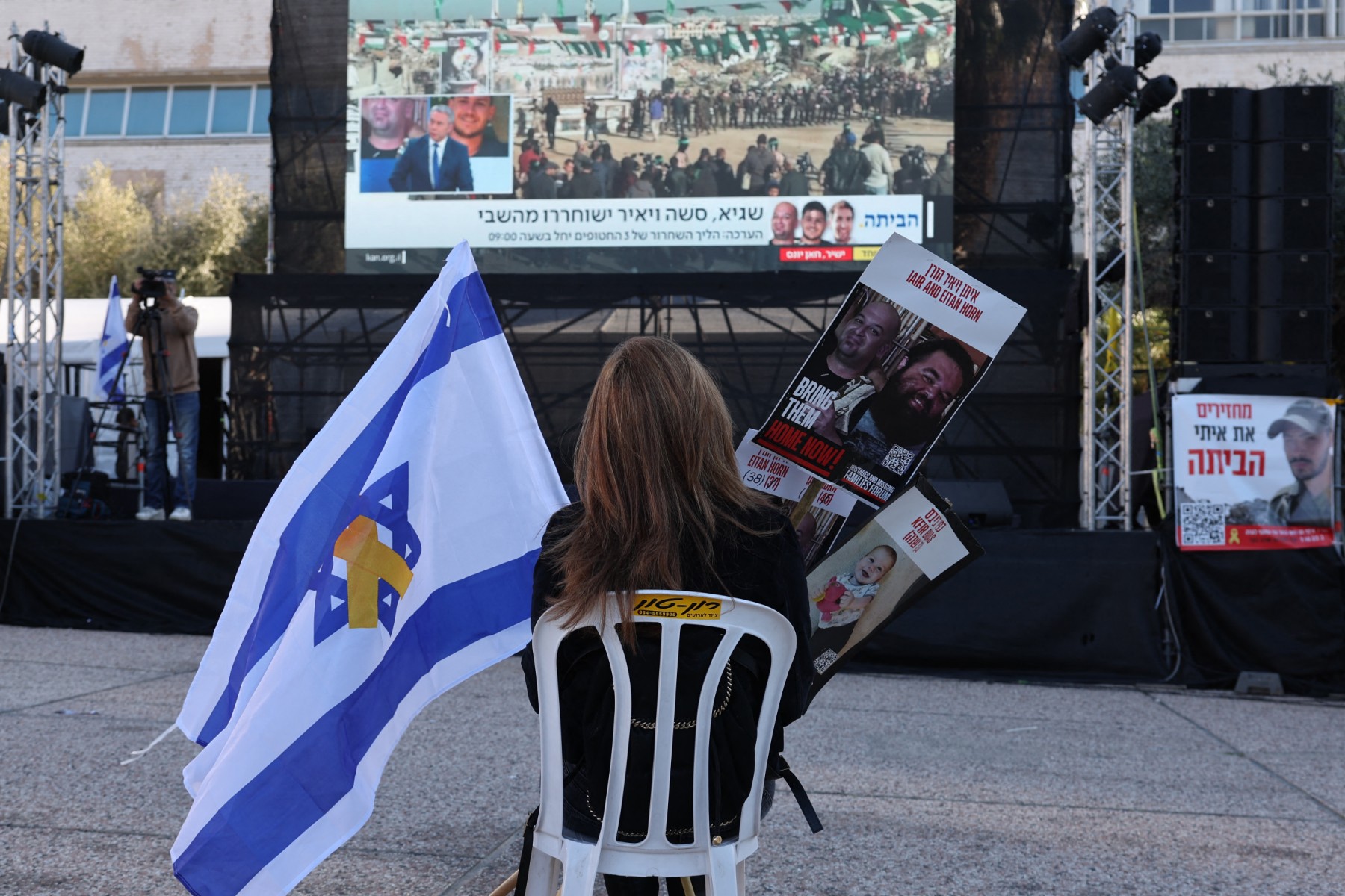A woman sits on a char in front of a screen in Tel Aviv's “Hostages Square”, holding an Israeli flag and pictures of hostages as families wait, Feb. 15, 2025. (AFP)
