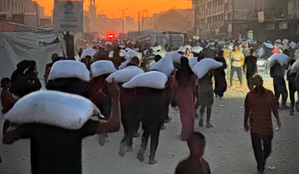Men walk carrying sacks of flour that were taken from a raided truck carry sacks of flour after raiding a truck that was carrying foodstuffs, in Khan Yunis in the southern Gaza Strip on July 22, 2025. (AFP)