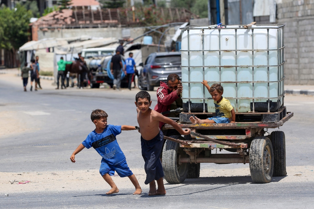 A man and young children push on a cart carrying a water tank at the Bureij camp for displaced Palestinians in the central Gaza Strip. (AFP)