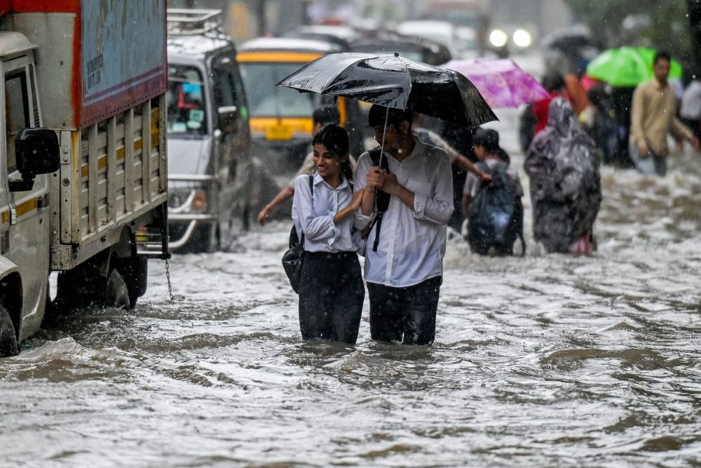 People wade through a flooded street during heavy rain showers in Mumbai on Aug. 18, 2025. (AFP)