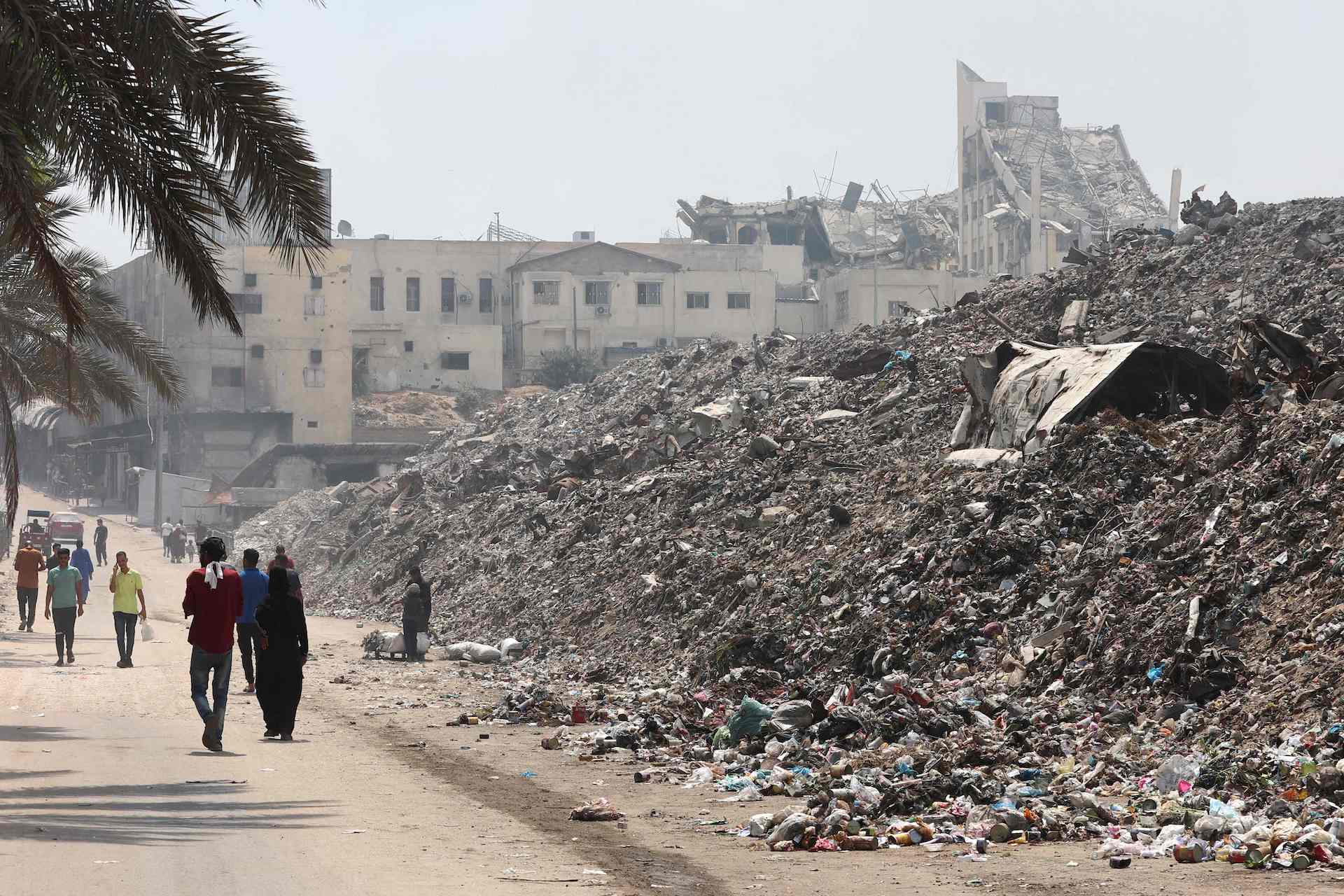 Palestinians walk past a garbage waste dump in Gaza City on August 18, 2025. (AFP)