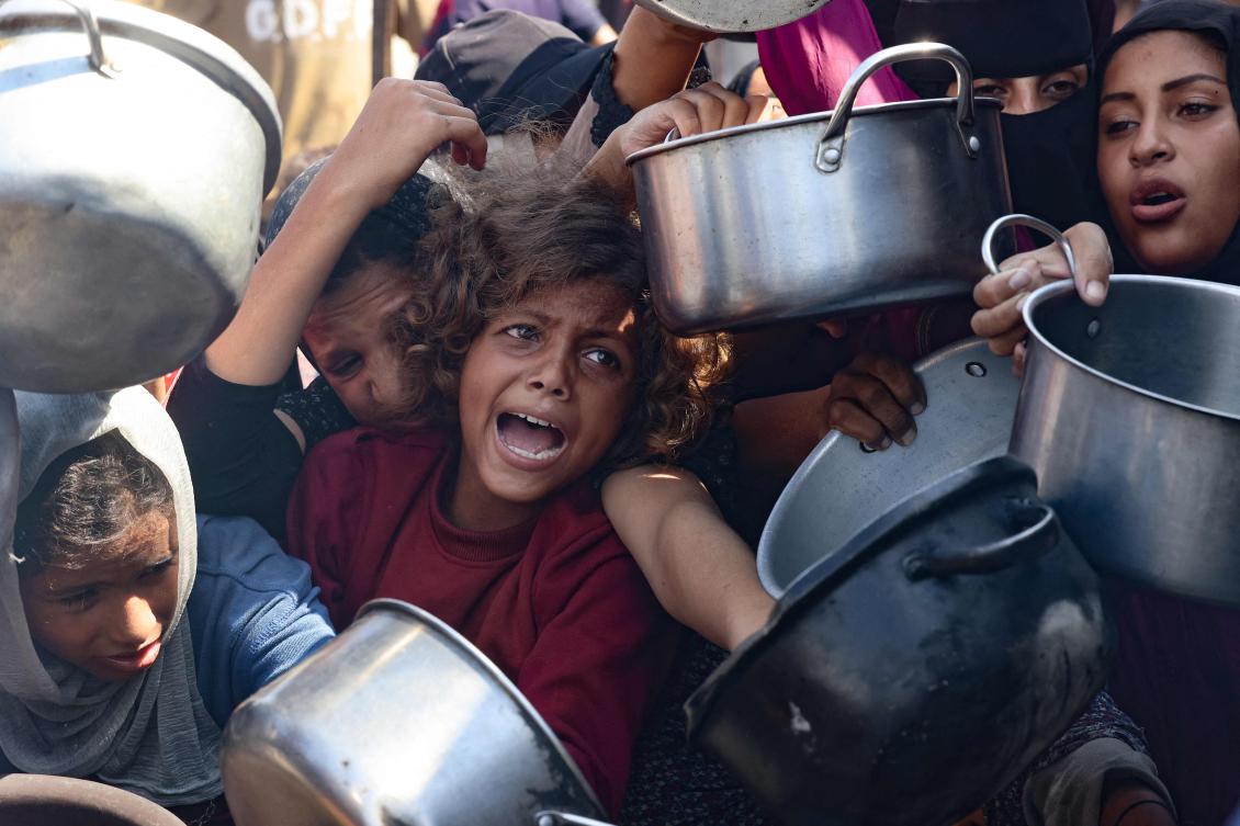 Palestinian women and children hold out their empty pots in front of a charity kitchen in Khan Yunis in the southern Gaza Strip on August 21, 2025. (AFP)