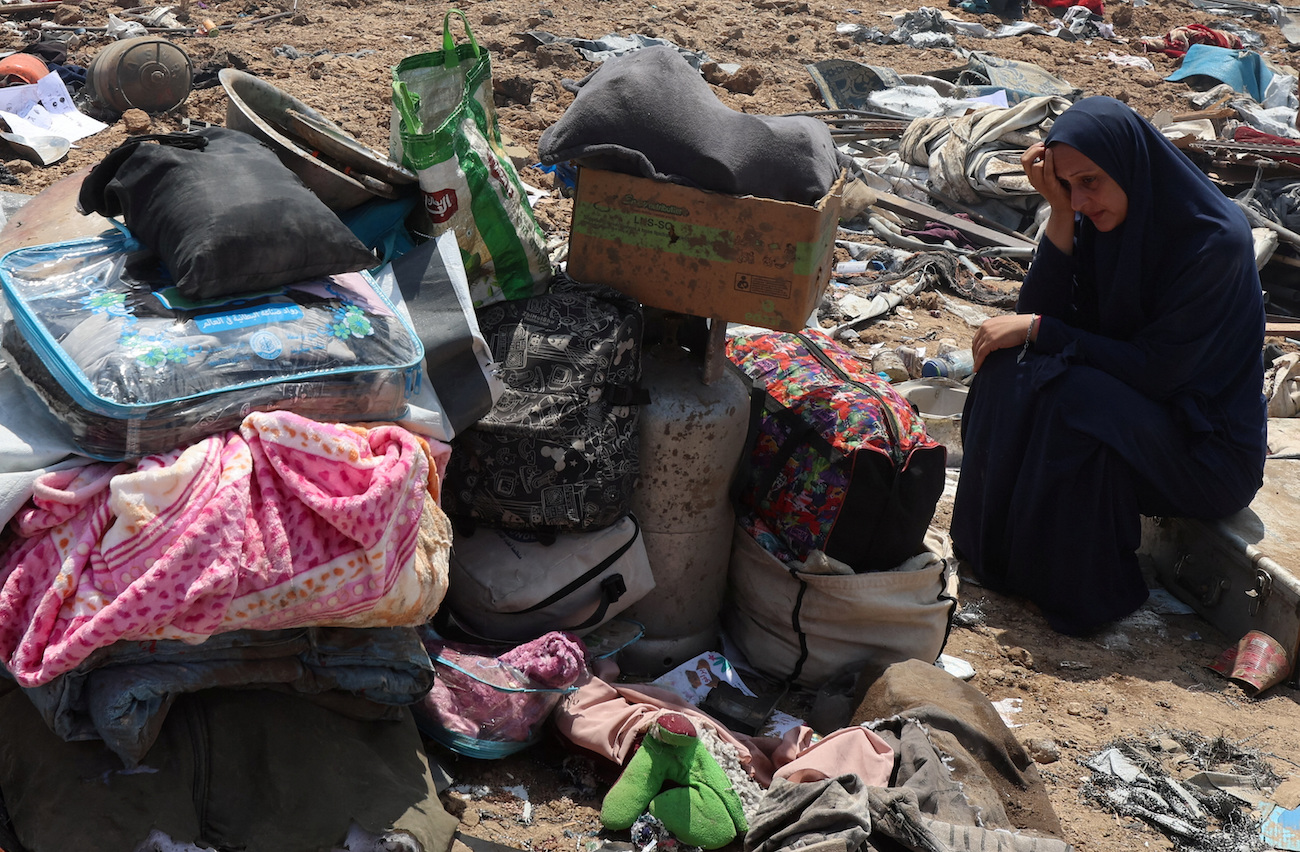 Palestinian woman sits next to belongings at the site of an Israeli strike on a tent camp sheltering displaced people, in Deir Al-Balah, in central Gaza Strip, August 21, 2025. (Reuters)