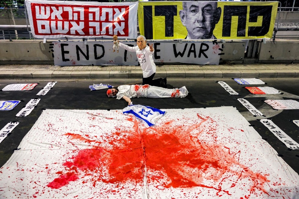 A demonstrator poses above another lying on the ground while depicting an Israeli hostage, during an anti-government protest in Tel Aviv. (AFP)