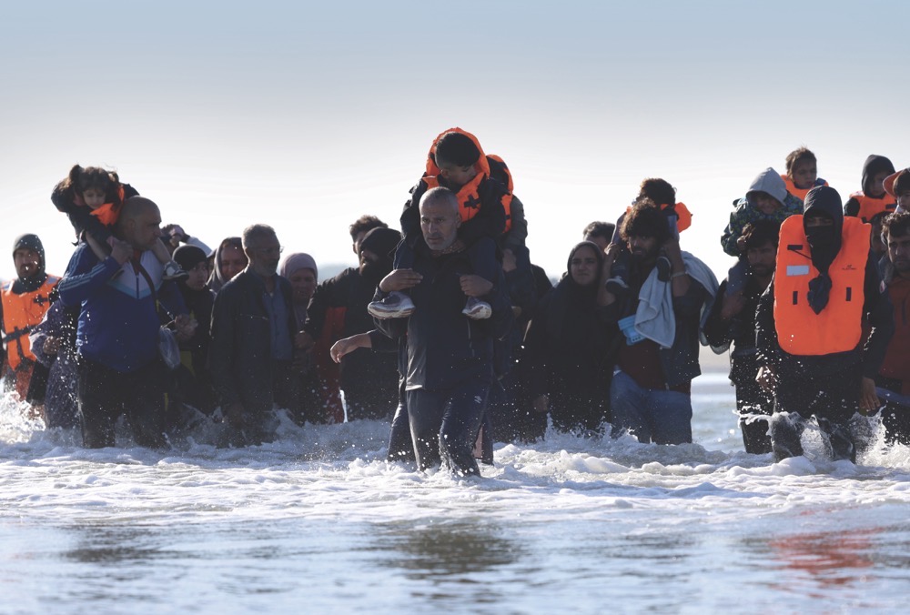 Migrants wade through the sea in an attempt to board a dinghy leaving the coast of northern France to cross the English Channel to reach Britain. (Reuters)