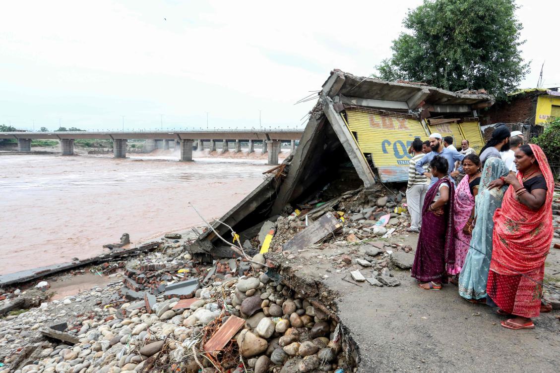 Residents gather near a damaged road along the banks of overflowing Tawi river after heavy rains induced flood in Jammu on Aug. 27, 2025. (AFP)