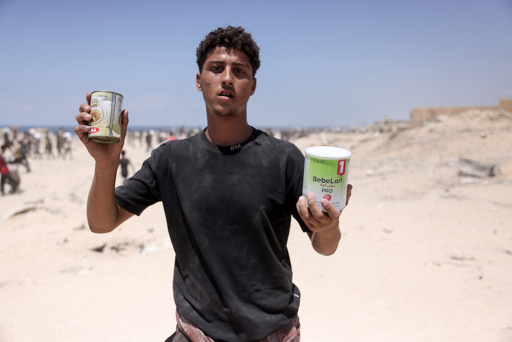 A Palestinian youth carries a can of food and a baby formula as he returns from an area in which aid trucks entered Gaza through the Zikim crossing point on Aug. 1, 2025. (AFP)