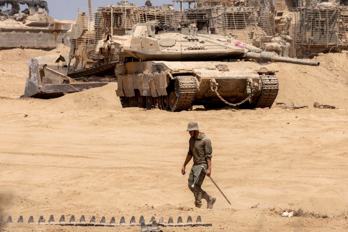 An Israeli army soldier walks near a main battle tank deployed at a position along the border with the Gaza Strip and southern Israel, July 29, 2025. (AFP)