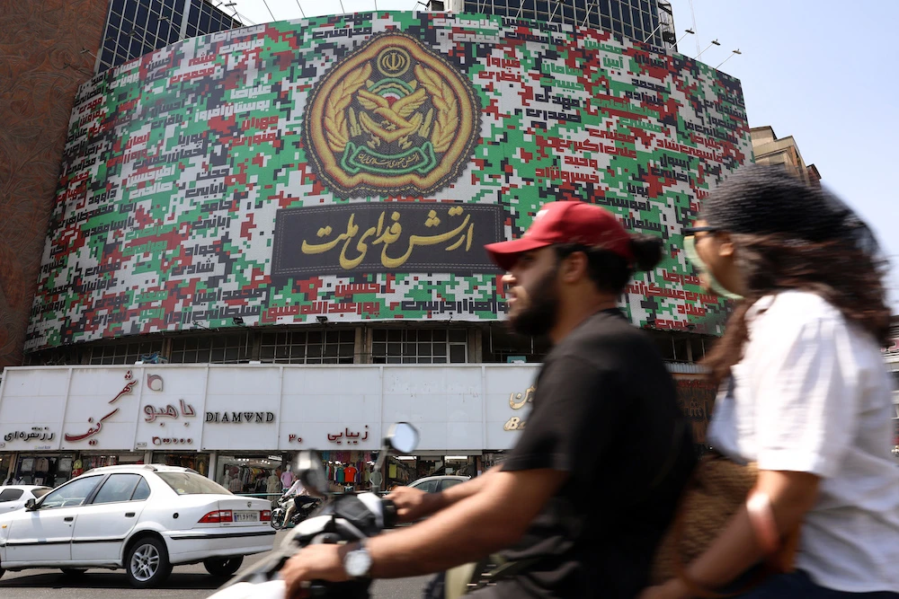 Iranians drive past a billboard with the colors of Iran’s national flag at the Valiasr square in Tehran on Aug. 29 2025. (AFP)