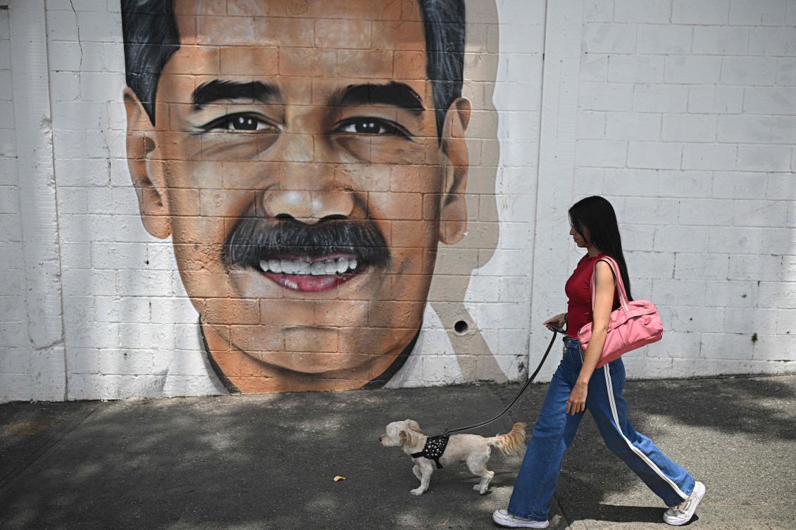 A woman walks her dog past a mural depicting Venezuela’s President Nicolas Maduro in Caracas on September 1, 2025. (AFP)