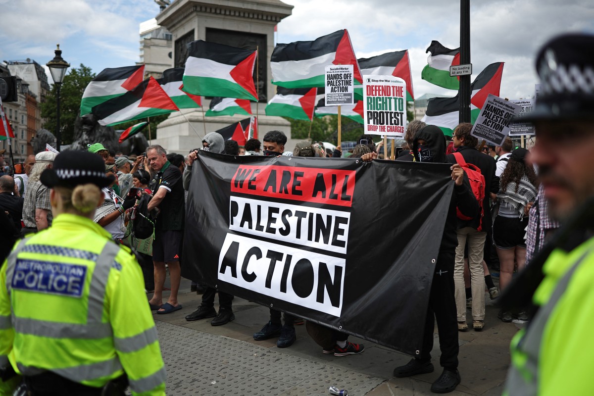 Police officers monitor protesters holding a banner during a protest in support of the Palestine Action group, before its official ban, in Trafalgar Square, London, June 23, 2025. (AFP)