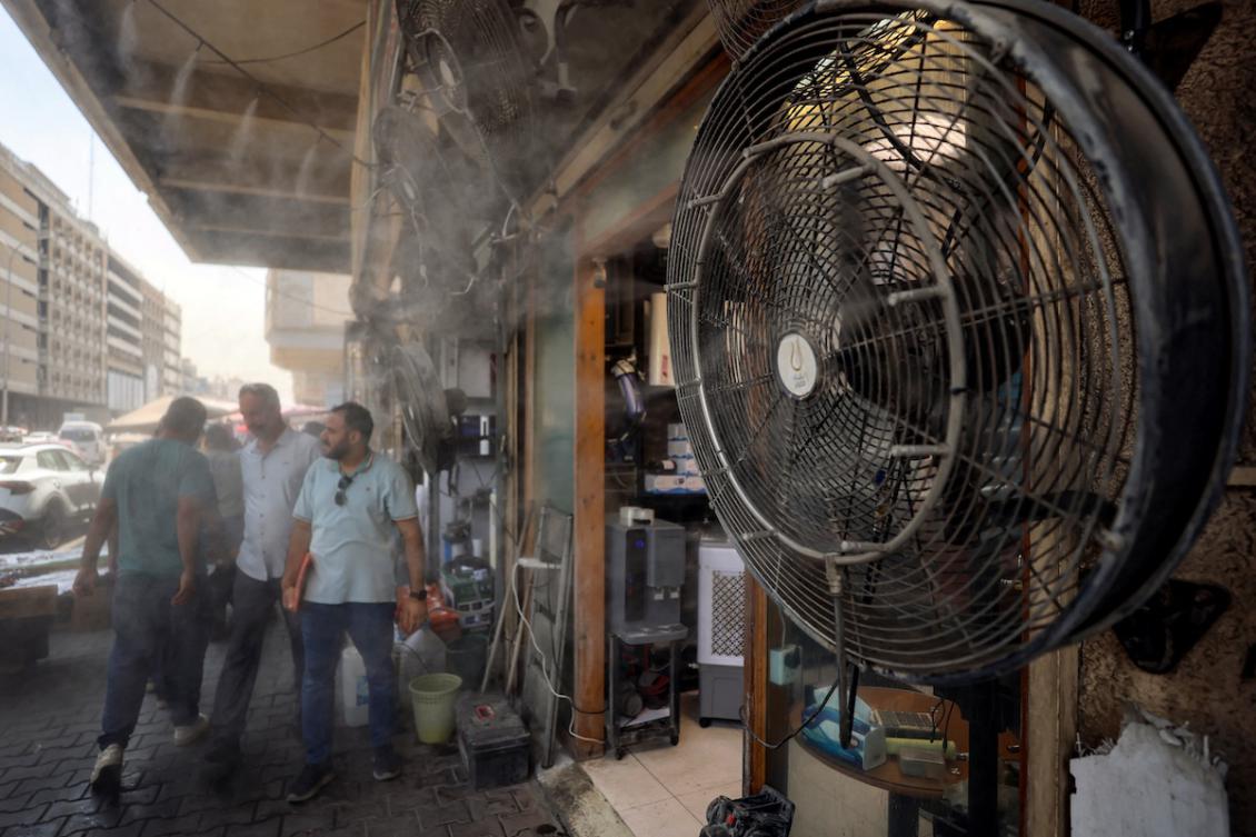 Pedestrians walk past 'water spray fans' placed along the side of a the road on al-Sinak street in central Baghdad amid rising temperatures on July 27, 2027 during a severe heatwave. (FILE/AFP)