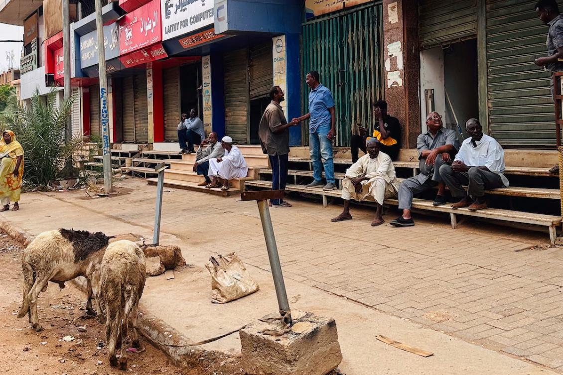 People sit on stairs outside shuttered stores at al-Hurriya street, a popular destination to buy electric home appliances before the Sudan war, as the shopping street reopens at al-Arabi market in Khartoum on July 15, 2025. (FILE/AFP)