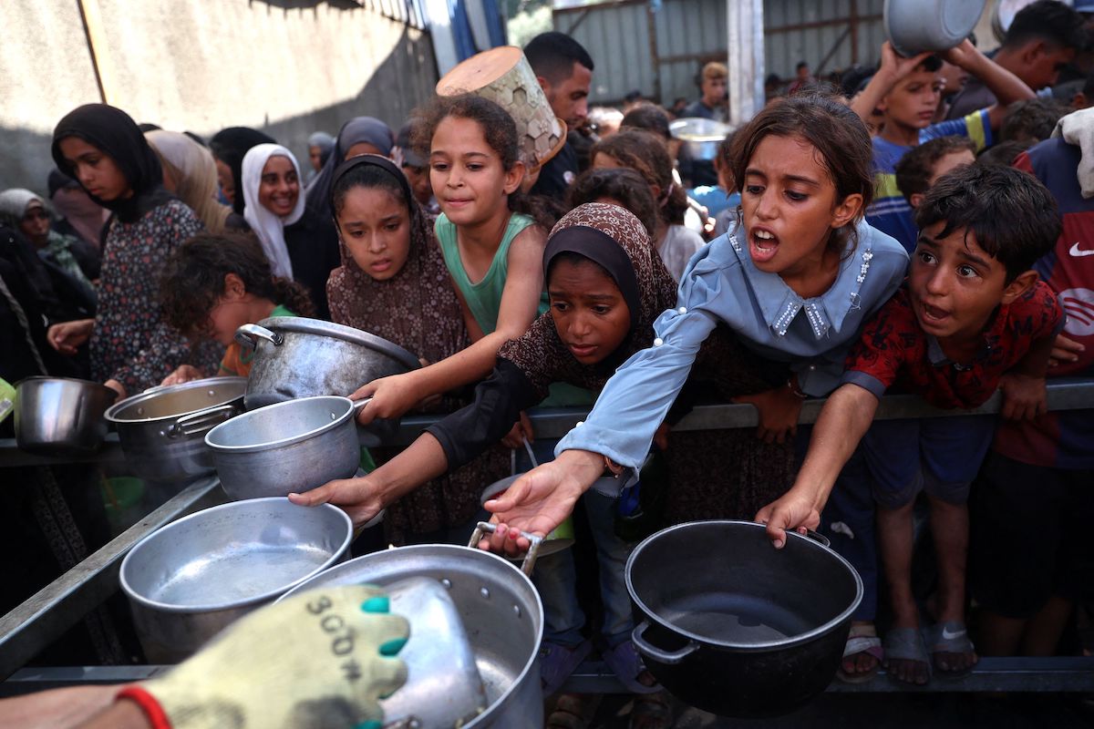 Palestinian children hold out their pans in front of a charity kitchen in the Nuseirat refugee camp in the central Gaza Strip on Sunday. (AFP)