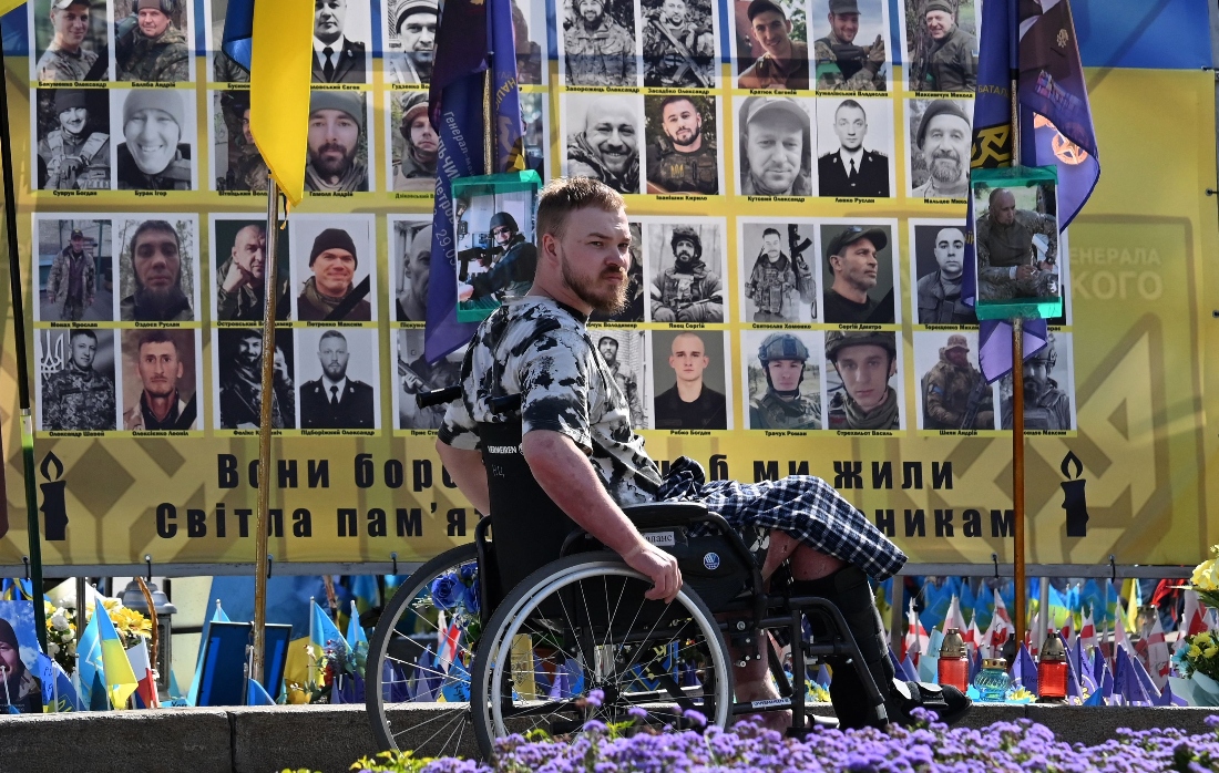 A wounded Ukrainian serviceman rides in a wheelchair at a makeshift memorial for fallen Ukrainian and foreign soldiers on Independence Square in Kyiv, Ukraine. (AFP)