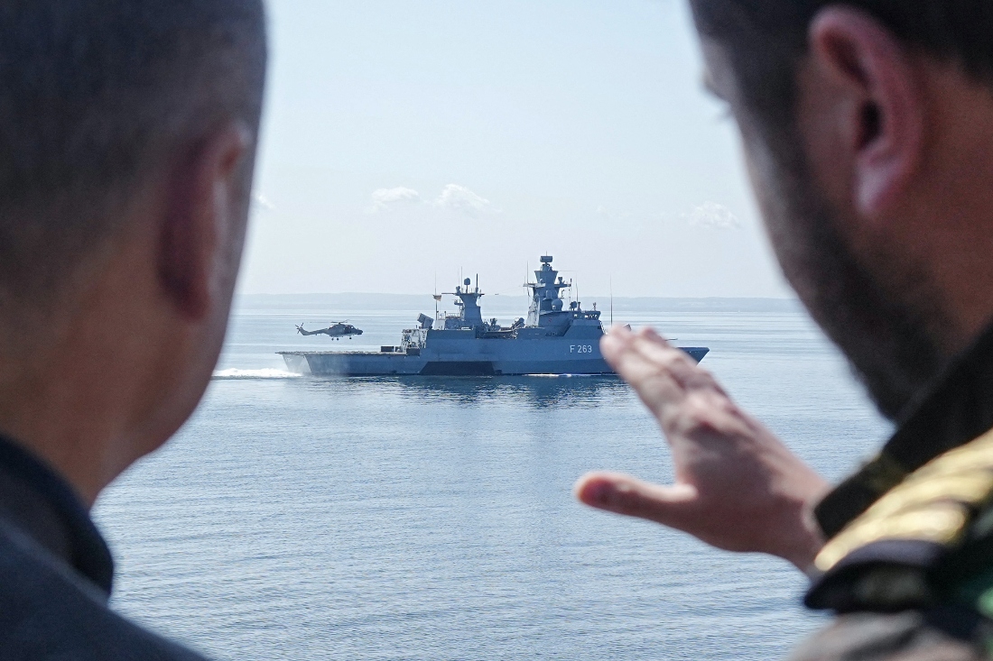 German Chancellor Olaf Scholz peaks with a serviceman as he stands aboard the frigate 'Mecklenburg-Vorpommern' during a military maneuver in the Baltic Sea at sea off Rostock-Warnemünde, northeastern Germany. (AFP)