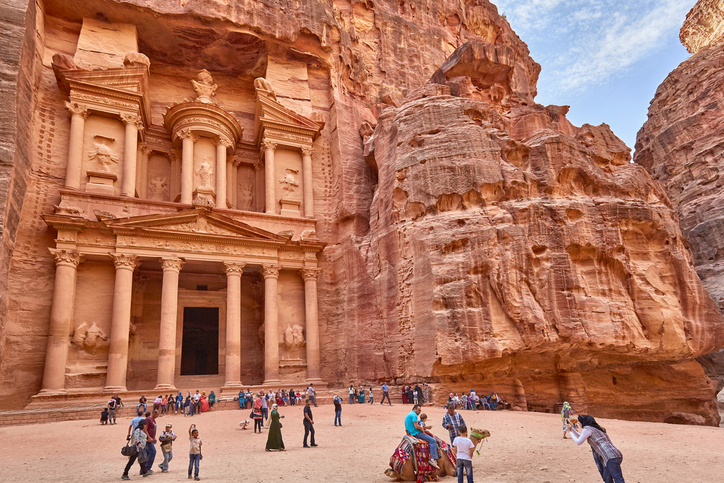 Tourists looking at the Treasury of Petra and taking photos with the camels. Getty
