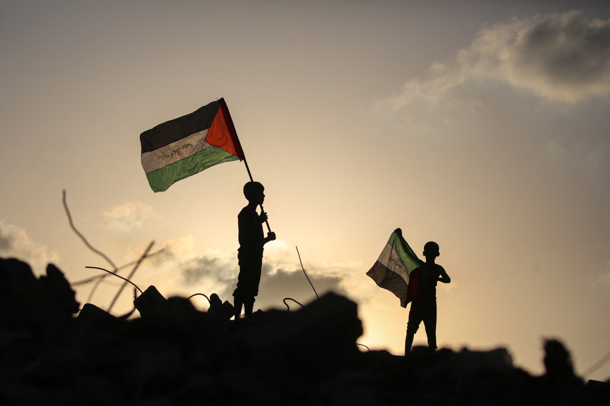 Displaced Palestinian children wave Palestinian national flags as they stand on the rubble of a destroyed building at the Bureij camp for refugees. (AFP)