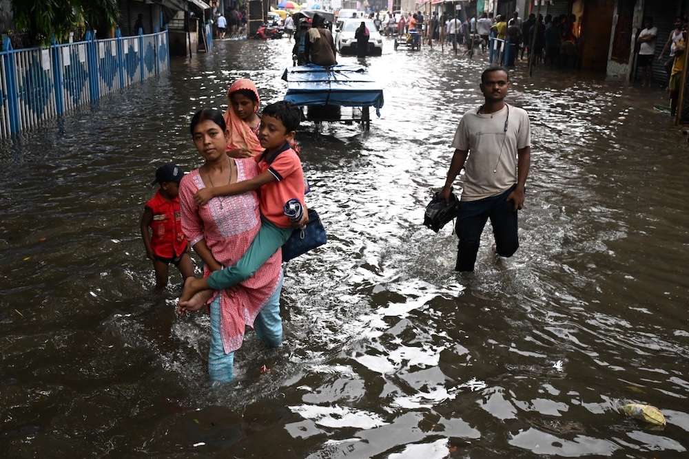 Commuters wade across a waterlogged street after heavy monsoon rains in Kolkata on Sept. 23, 2025. (AFP)
