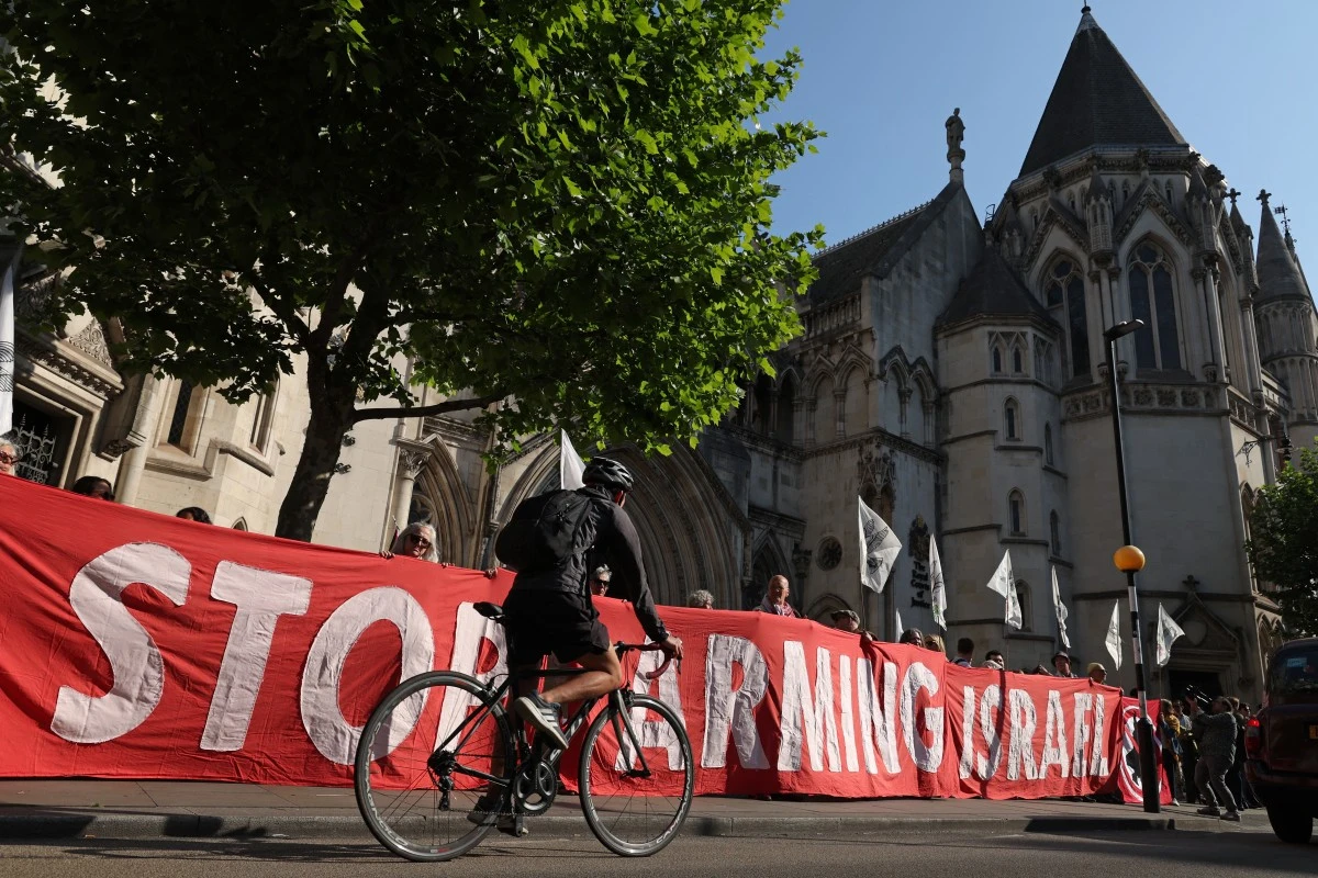 A cyclist rides past a group of pro-Palestinian activists and supporters holding a large banner outside the Royal Courts of Justice in central London on May 13, 2025, ahead of a court hearing on the UK government's supply of arms to Israel. (AFP)