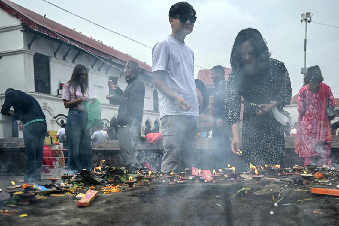 Hindu devotees light oil lamps outside the Pashupatinath Temple in Kathmandu on September 14, 2025. The capital Kathmandu took a step back towards normality on September 13 as a curfew was eased and daily life returned, with markets opening, traffic returning and families visiting temples. (Photo by Arun SANKAR / AFP)