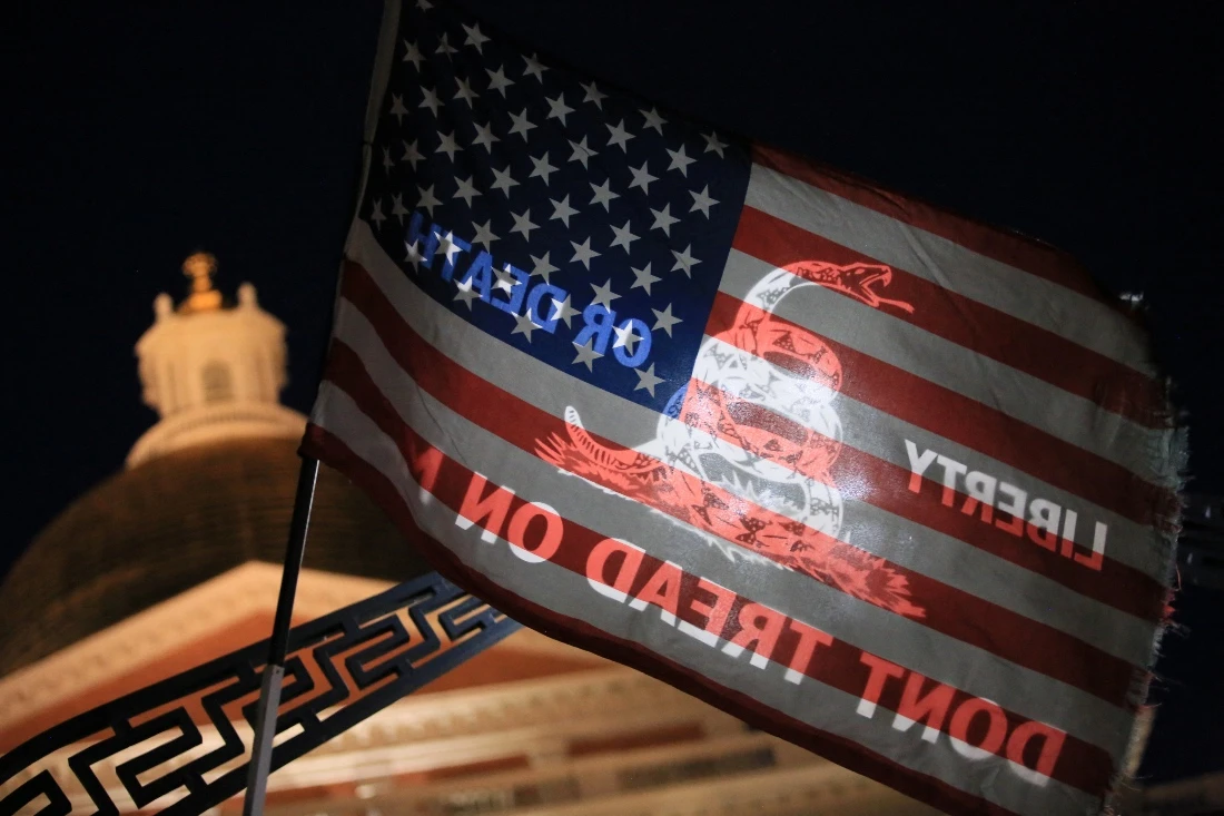 A flag with the U.S. flag on one side, and a variation of the "Don't Tread on Me" flag on the other, is held in front of the State House during a prayer vigil for Charlie Kirk in Boston, US.