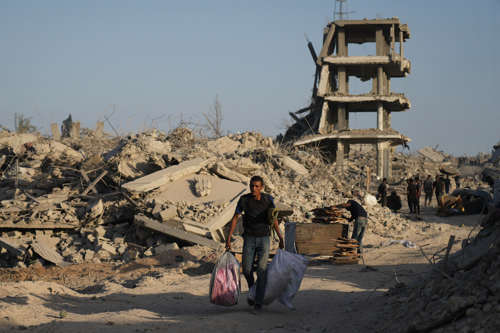 A displaced Palestinian man carries his belongings as he walks past destroyed buildings. (AP)