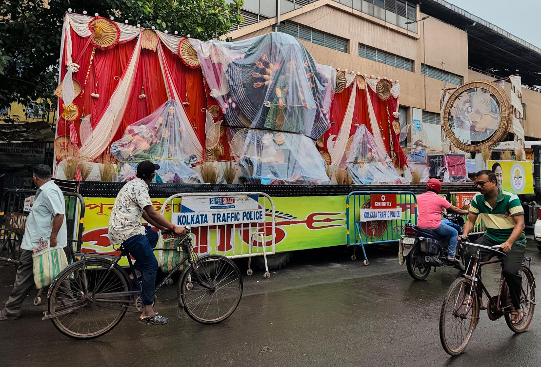 Commuters pass an idol of Hindu goddess Durga on a parked truck, wrapped in plastic sheets awaits immersion, in Kolkata, India, Sunday, Oct. 5, 2025. (AP Photo/Bikas Das)