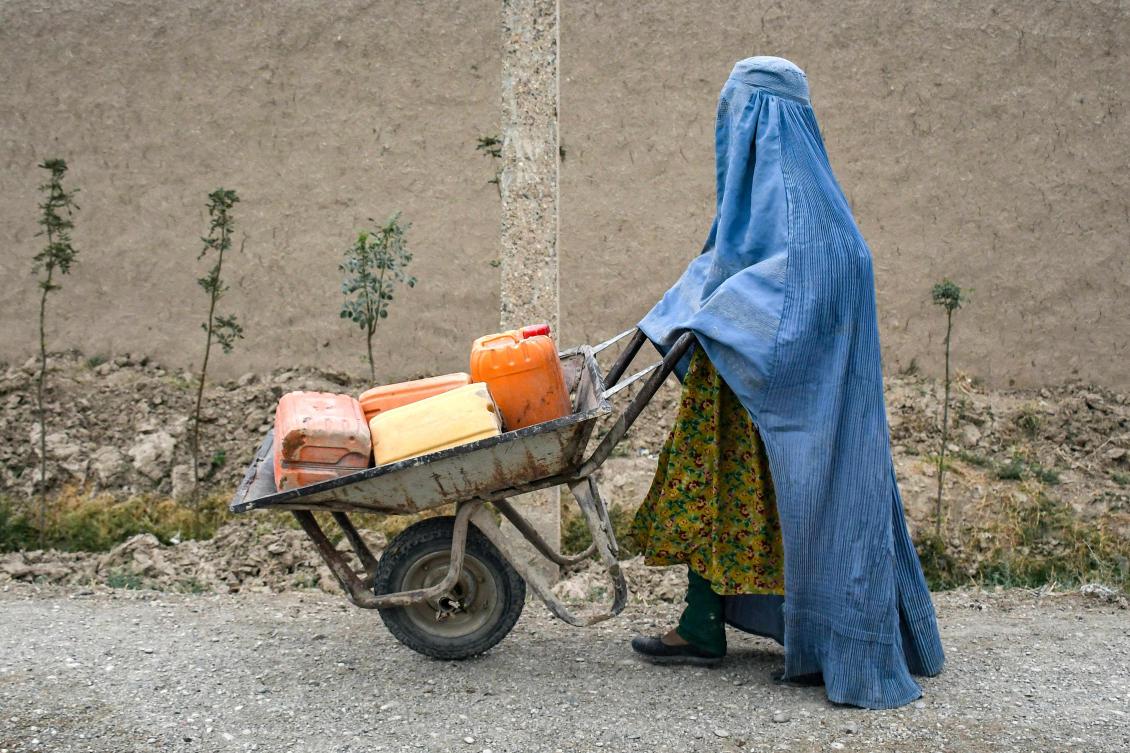 An Afghan burqa-clad woman pushes a wheelbarrow loaded with empty water canisters as she walks along a street in the Koshkak area of the Balkh province on October 5, 2025. (AFP)