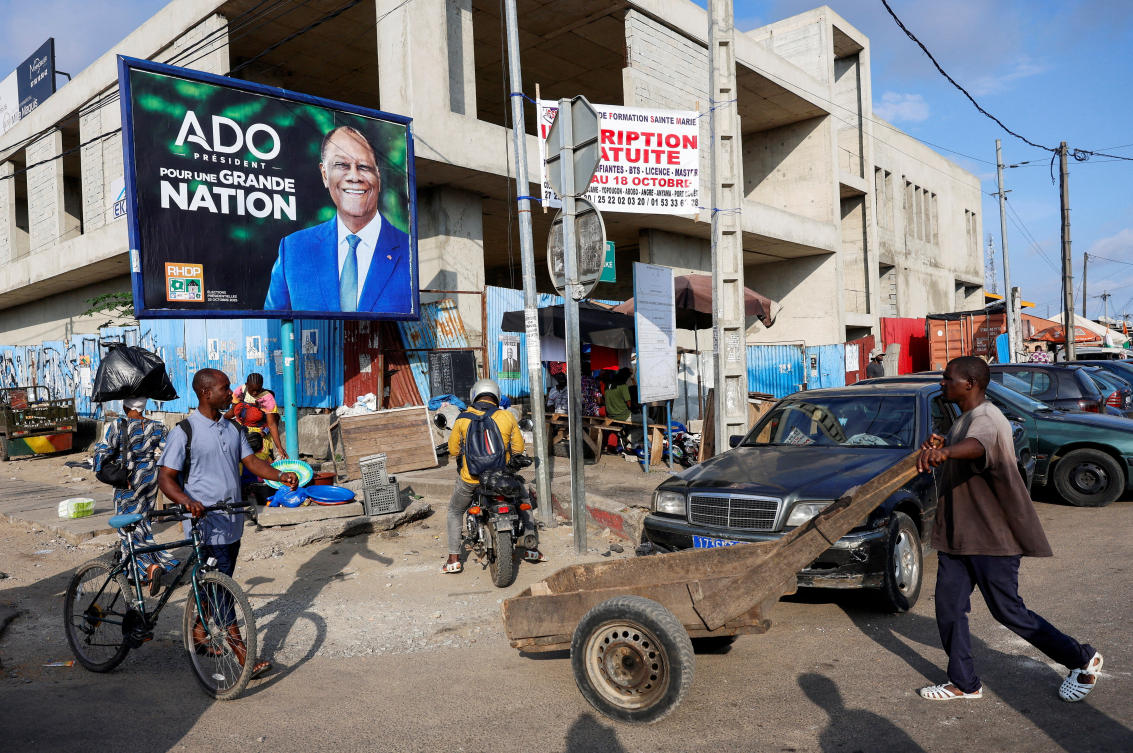 People move next to a campaign billboard of Ivory Coast’s President Alassane Ouattara, 83, who is seeking a fourth term, ahead of Ivory Coast presidential election scheduled on Oct. 25 in Abidjan, Oct. 10, 2025. (Reuters)
