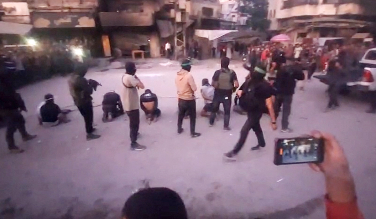 This image grab from a handout video released by the Hamas-run al-Aqsa TV's Telegram channel on October 13, 2025, shows armed Hamas fighters standing behind blindfolded, bound and kneeling men as a crowd surrounds them in a street in Gaza City. (AFP)