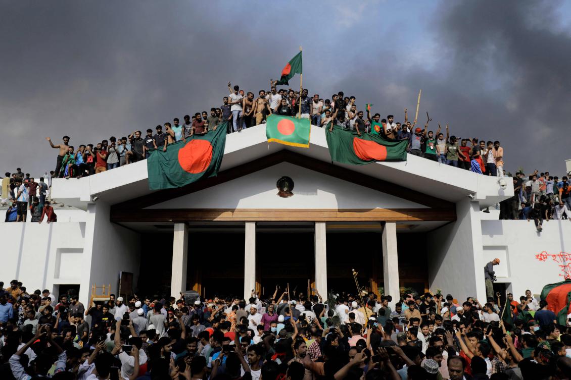Anti-government protestors display Bangladesh's national flag as they storm Prime Minister Sheikh Hasina's palace in Dhaka on August 5, 2024. (Photo by K M ASAD / AFP)