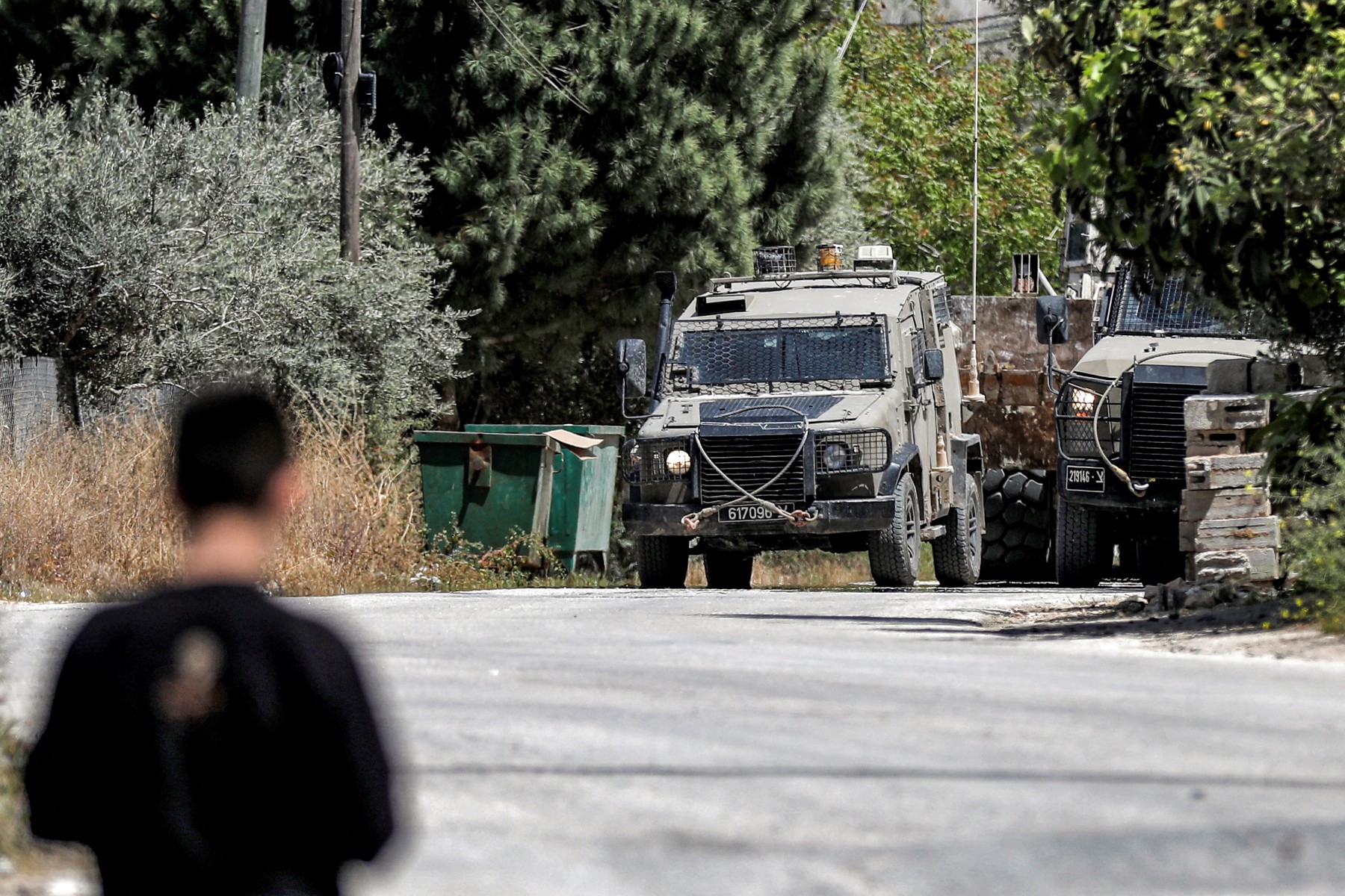 A man looks on as Israeli military armored vehicles are pictured during an army operation in the village of al-Misliyah, south of Jenin in the northern occupied West Bank, Apr. 16, 2025. (AFP)